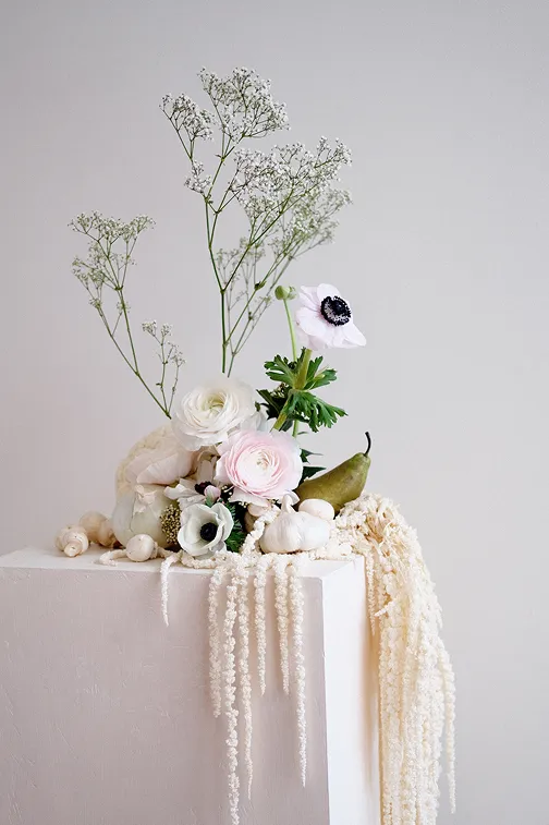 une composition florale avec une poire au milieu des fleurs, pleureuses de couleur blanche, accompagnant ce magnifique bouquet de fleurs roses et blanches