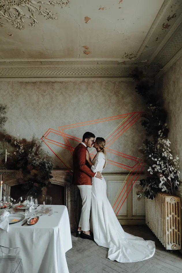 dans un décor vétuste composé de blanc et de fleurs, mise en scène pour le côté artistique, un couple marié vêtu d’habits de mariage — robe pour la femme et costume pour le mari — le visage collé l’un à l’autre