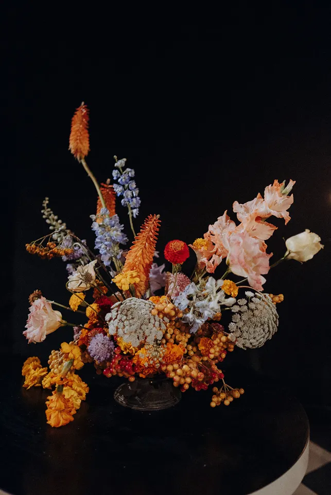 sur un fond noir se trouve un bouquet de fleurs composé de couleurs vives, comprenant l’orange, le bleu et le rose