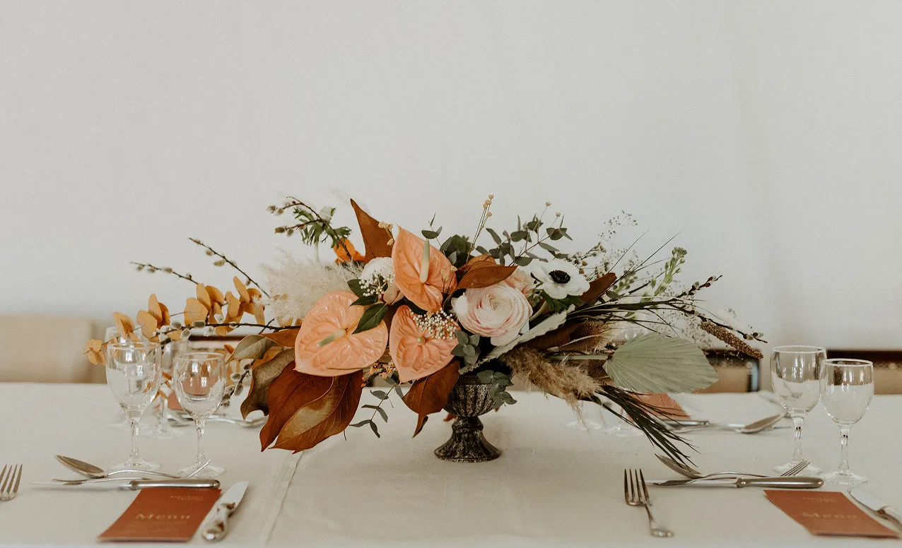sur une table dressée se trouve un vase contenant un bouquet de fleurs composé des couleurs rose et rose pâle