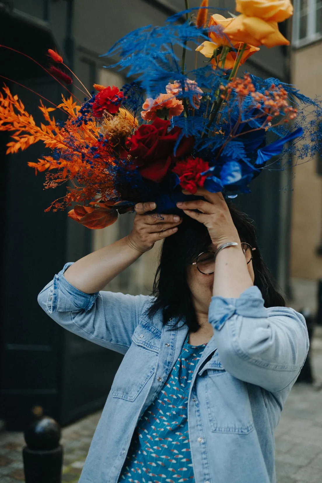 une fleuriste tient au-dessus d’elle un bouquet de fleurs bleues, orange et jaunes