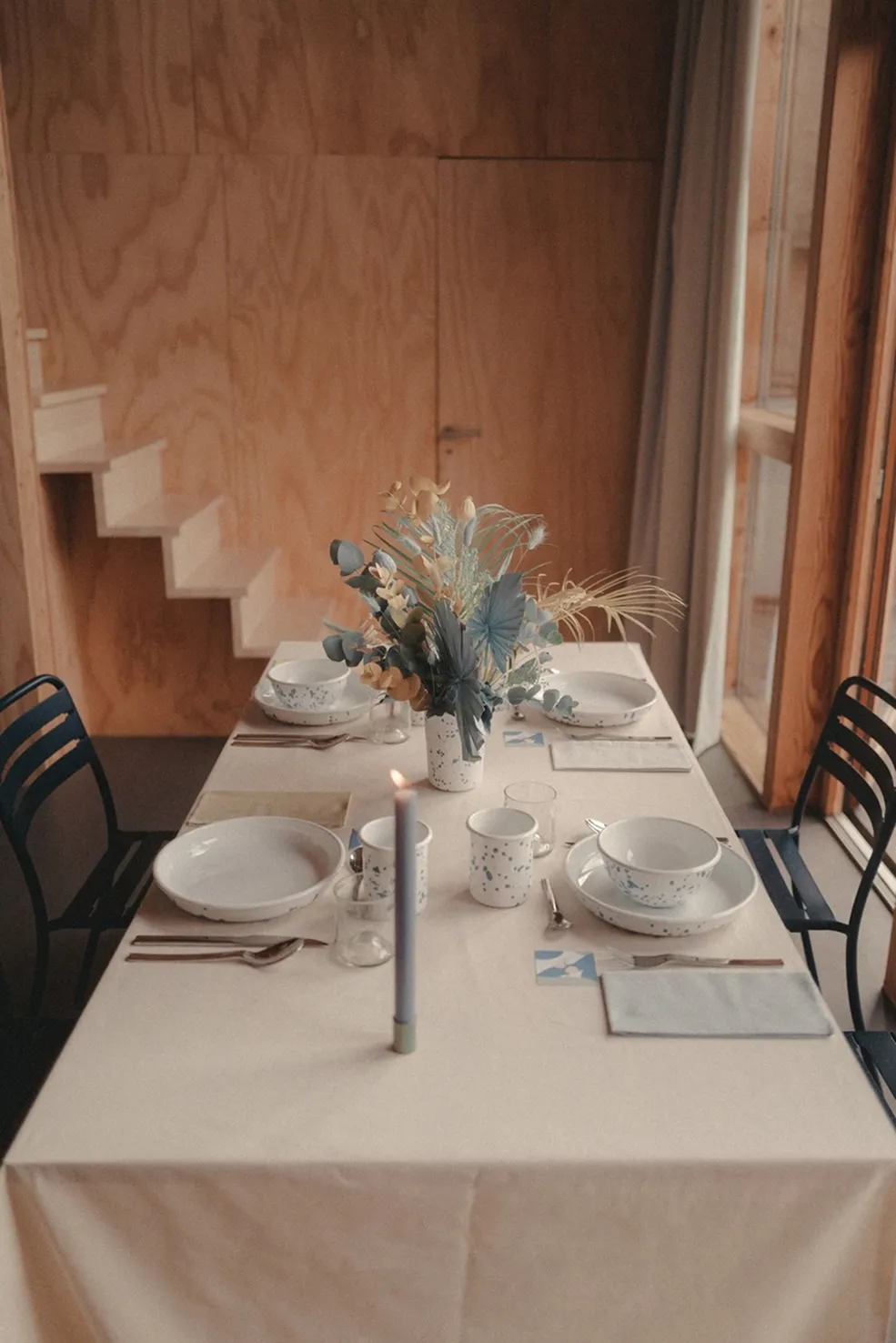 sur une table se trouvent quatre assiettes et couverts, avec un petit vase rempli de fleurs bleues, dorées et des fleurs dorées