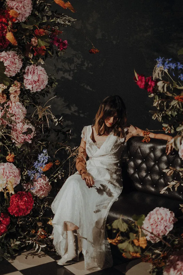 entourée de plusieurs fleurs se trouve une femme assise vêtue d’une robe de mariée