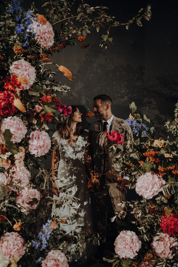 un couple de mariés en arrière-plan et au premier plan se trouvent diverses fleurs de couleur rose, rouge et jaune