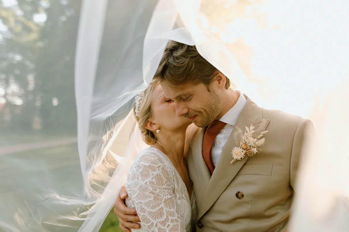un couple de mariés derrière un voile s’embrassant